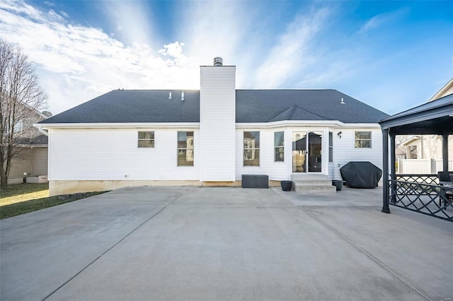 back of house featuring entry steps, fence, roof with shingles, a chimney, and a patio area