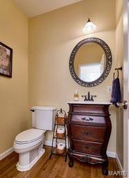 half bath featuring vanity, toilet, wood finished floors, and baseboards