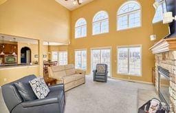 carpeted living room with a stone fireplace and lofted ceiling