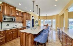 kitchen featuring stainless steel microwave, glass insert cabinets, light countertops, black electric cooktop, and a kitchen island with sink