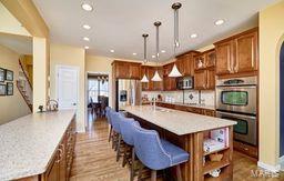 kitchen featuring double oven, brown cabinetry, refrigerator with ice dispenser, and light countertops