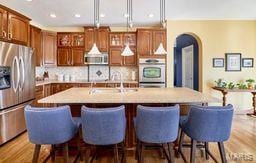 kitchen with a center island with sink, appliances with stainless steel finishes, wood finished floors, arched walkways, and a sink