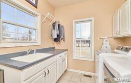 laundry room featuring washer and dryer, a sink, cabinet space, light tile patterned floors, and baseboards