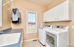 laundry area featuring light tile patterned floors, a sink, cabinet space, and separate washer and dryer