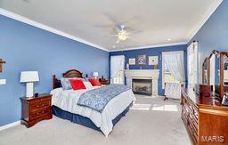 carpeted bedroom with a fireplace with raised hearth, baseboards, and ornamental molding