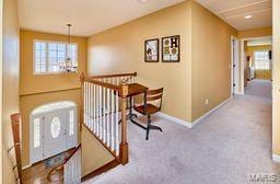 hall with carpet flooring, baseboards, a wealth of natural light, and a chandelier