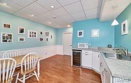 kitchen with beverage cooler, light countertops, wood finished floors, a paneled ceiling, and a sink