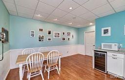 dining space featuring a paneled ceiling, a wainscoted wall, wine cooler, and wood finished floors