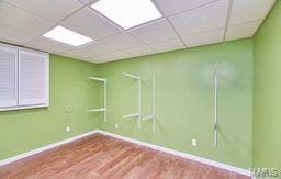 spare room with baseboards, a paneled ceiling, and wood finished floors