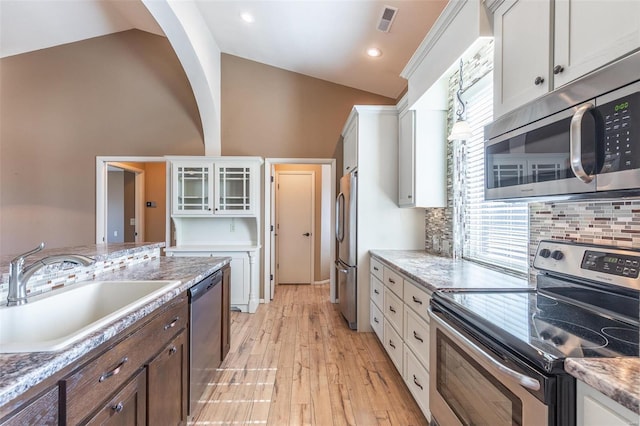 kitchen with vaulted ceiling, stainless steel appliances, a sink, and white cabinets