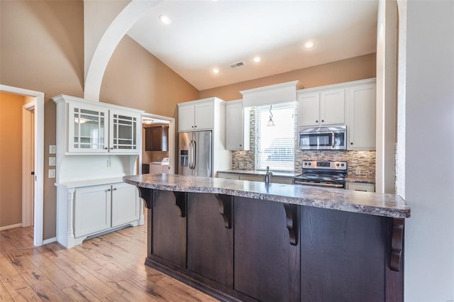 kitchen with stainless steel appliances, a breakfast bar, white cabinets, and vaulted ceiling