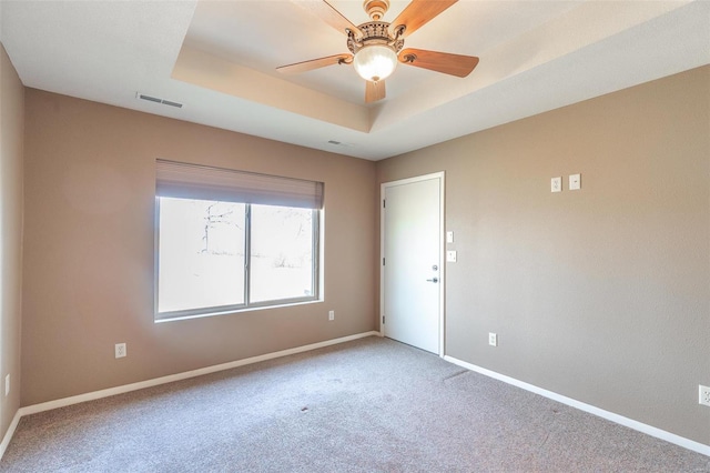 carpeted spare room with a tray ceiling, visible vents, ceiling fan, and baseboards