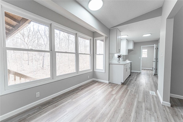 kitchen featuring visible vents, light countertops, lofted ceiling, light wood-style floors, and a textured ceiling