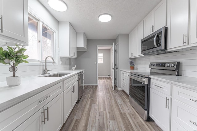 kitchen featuring light wood-style flooring, a sink, decorative backsplash, stainless steel appliances, and white cabinets