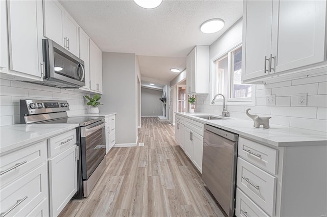 kitchen with white cabinets, light wood-style flooring, appliances with stainless steel finishes, and a sink