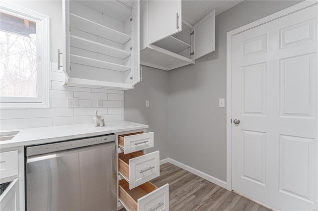 kitchen featuring backsplash, stainless steel dishwasher, light countertops, and white cabinetry