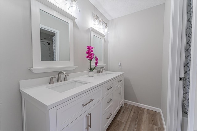 full bathroom featuring double vanity, wood finished floors, a textured ceiling, and a sink