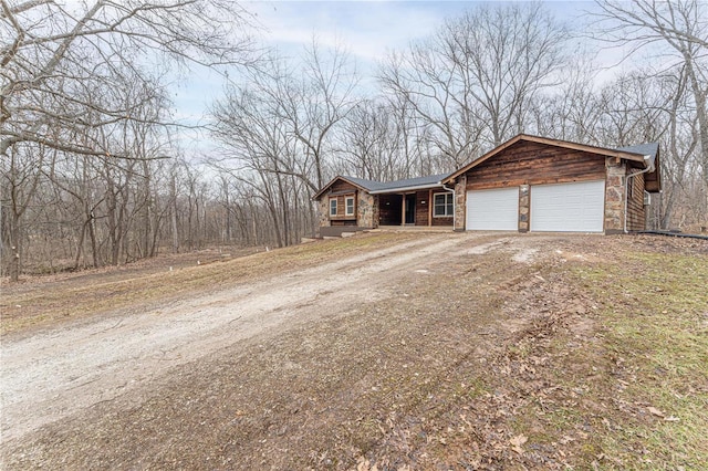 view of front of house with stone siding, an attached garage, and dirt driveway