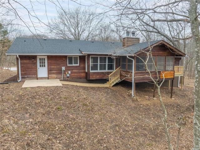 rear view of property featuring a chimney, a patio area, a shingled roof, and a sunroom