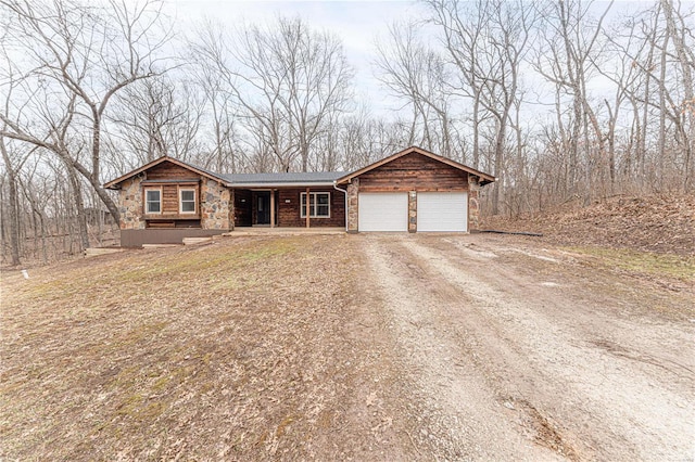 view of front of home featuring stone siding, an attached garage, covered porch, and driveway