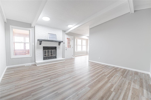 unfurnished living room with a brick fireplace, baseboards, light wood finished floors, and a textured ceiling