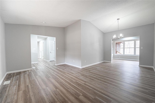 spare room with visible vents, baseboards, lofted ceiling, wood finished floors, and a notable chandelier