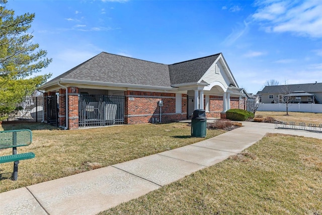 view of front facade with roof with shingles, fence, a front lawn, and brick siding