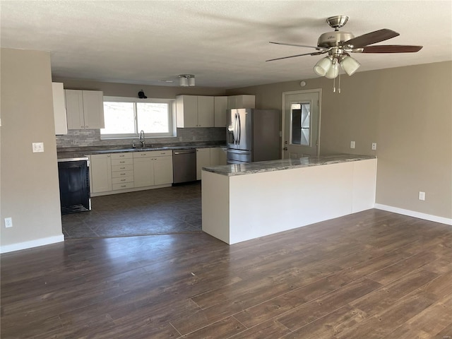 kitchen featuring dark wood finished floors, a peninsula, a sink, decorative backsplash, and appliances with stainless steel finishes