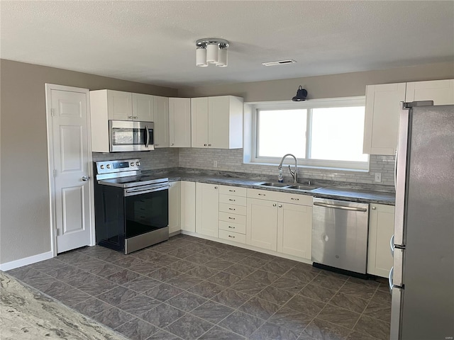 kitchen featuring a sink, tasteful backsplash, dark countertops, stainless steel appliances, and white cabinets