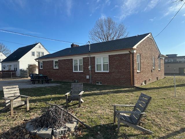 back of house featuring a patio, brick siding, a chimney, and a lawn