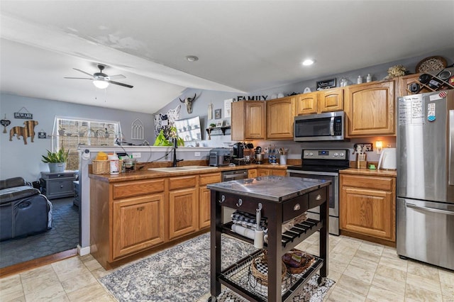 kitchen with a ceiling fan, appliances with stainless steel finishes, a peninsula, vaulted ceiling, and a sink