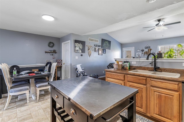 kitchen with lofted ceiling, stainless steel countertops, a sink, visible vents, and brown cabinets