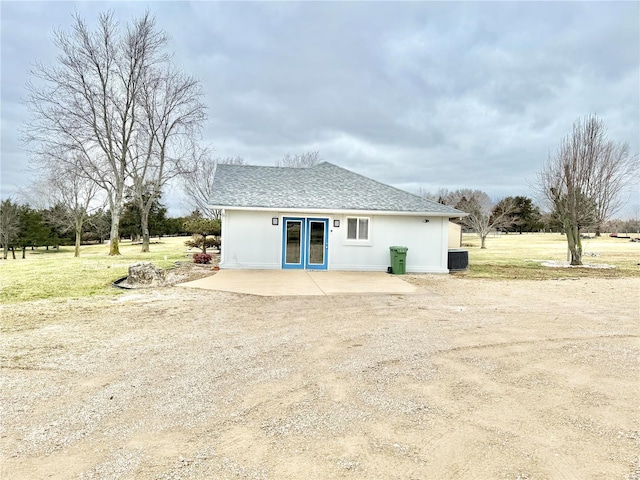 rear view of house featuring a patio, central AC unit, a shingled roof, french doors, and stucco siding