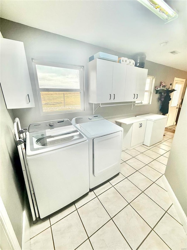 laundry area featuring washer and clothes dryer, light tile patterned flooring, cabinet space, and a healthy amount of sunlight