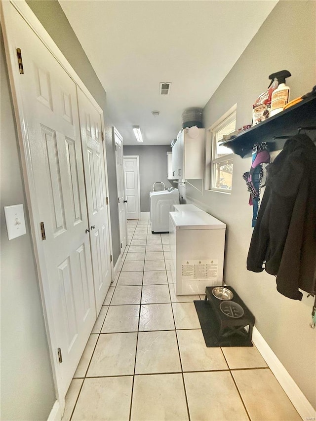 interior space featuring light tile patterned floors, visible vents, baseboards, cabinet space, and washer and clothes dryer