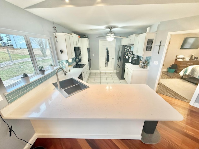 kitchen featuring a peninsula, a sink, white cabinetry, light countertops, and black appliances