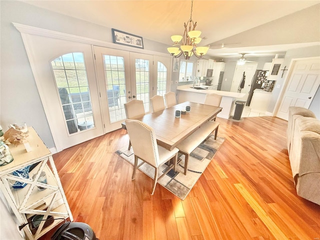 dining area featuring vaulted ceiling, french doors, light wood-style flooring, and an inviting chandelier