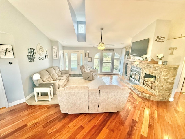 living room featuring vaulted ceiling, a fireplace, baseboards, and wood finished floors