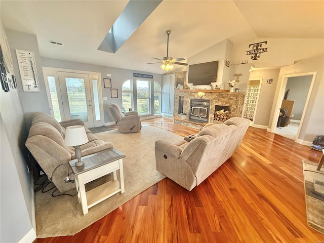 living room featuring visible vents, a stone fireplace, wood finished floors, vaulted ceiling with skylight, and baseboards