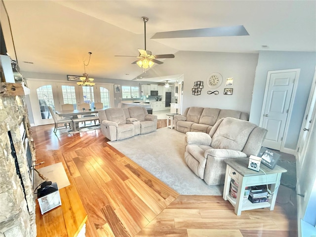 living room featuring lofted ceiling, a fireplace, light wood-style flooring, and a ceiling fan