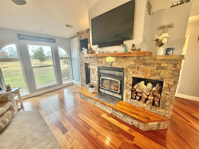 living area featuring high vaulted ceiling, a fireplace, wood finished floors, visible vents, and baseboards