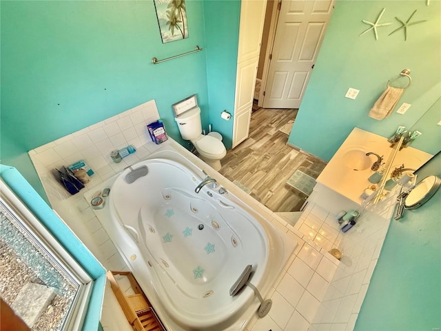 bathroom with a sink, toilet, a tub with jets, and wood finished floors