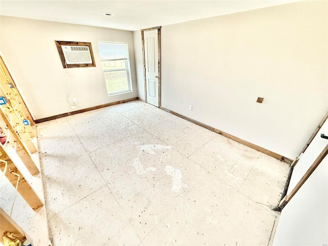 spare room featuring a wall unit AC and baseboards