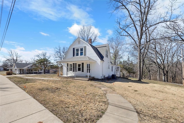 dutch colonial featuring a shingled roof, a gambrel roof, a chimney, a front lawn, and central AC