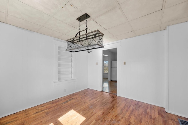 unfurnished dining area with built in features, visible vents, and hardwood / wood-style flooring