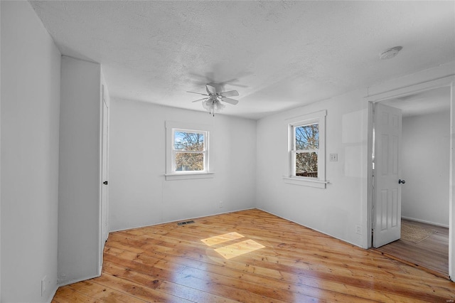 unfurnished room with a textured ceiling, light wood finished floors, visible vents, and a ceiling fan