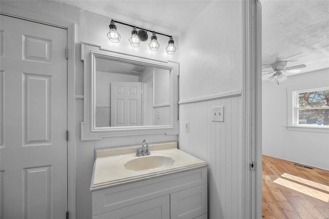 bathroom featuring a textured ceiling, hardwood / wood-style flooring, a wainscoted wall, visible vents, and a ceiling fan