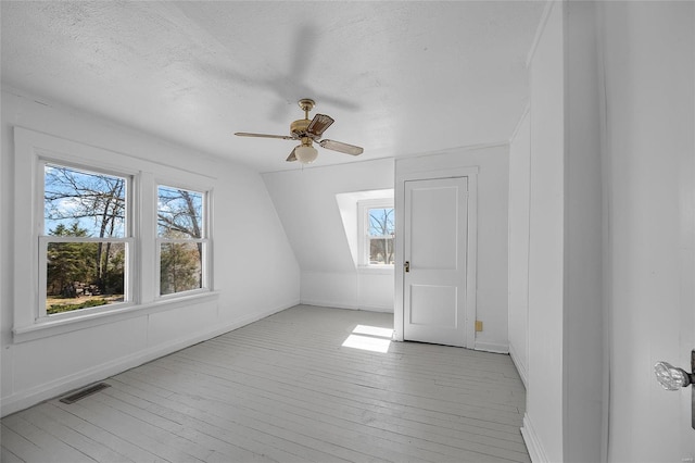 additional living space with lofted ceiling, ceiling fan, a textured ceiling, visible vents, and light wood finished floors