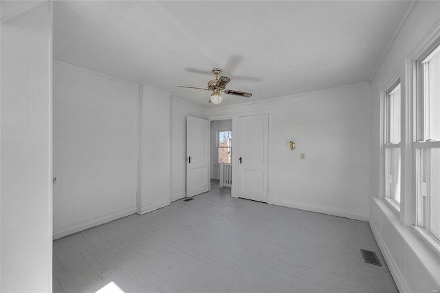 spare room featuring visible vents, a ceiling fan, ornamental molding, wood finished floors, and baseboards