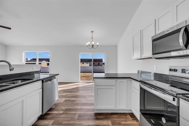 kitchen with a peninsula, a sink, white cabinets, appliances with stainless steel finishes, and an inviting chandelier